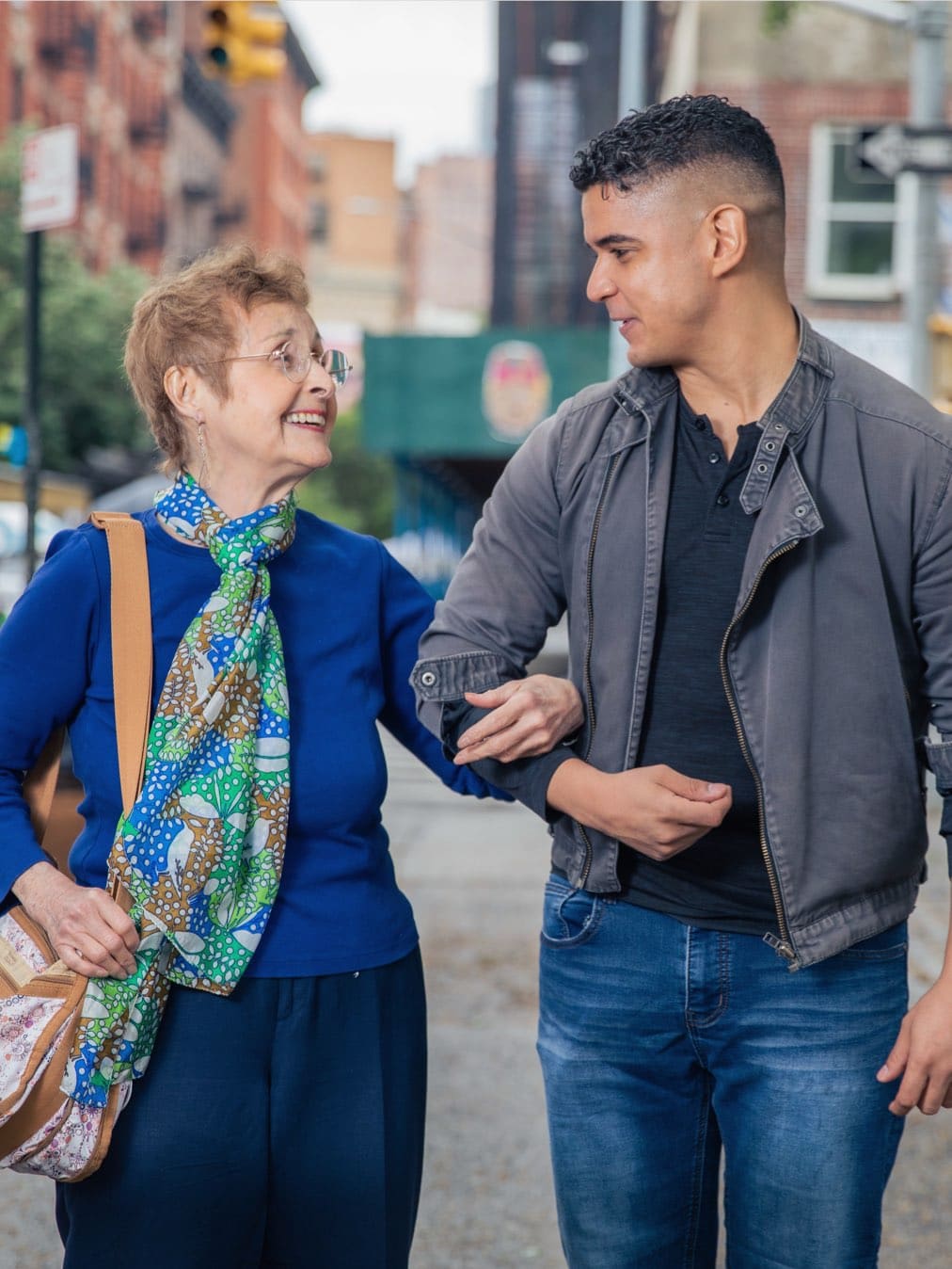 Male caregiver supporting elderly woman as they walk down the street
